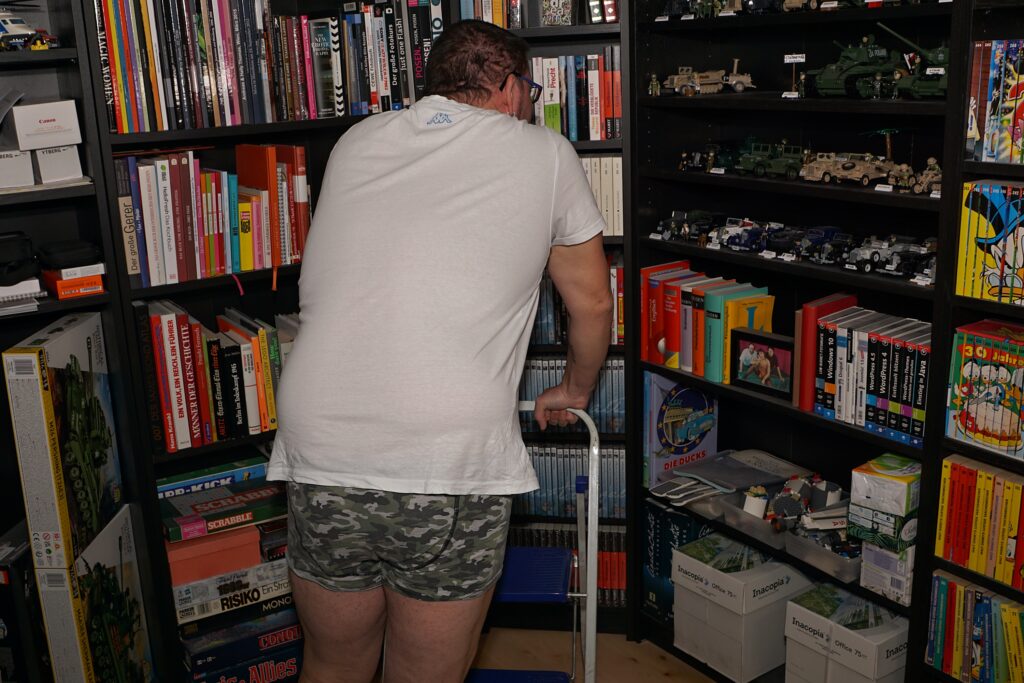 mit Unterhose und weißem T-Shirt vor einem Bücherregal