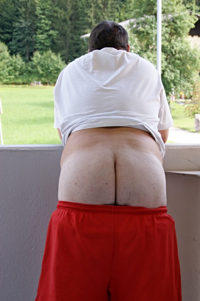 am Balkon stehend mit runter gelassener Hose